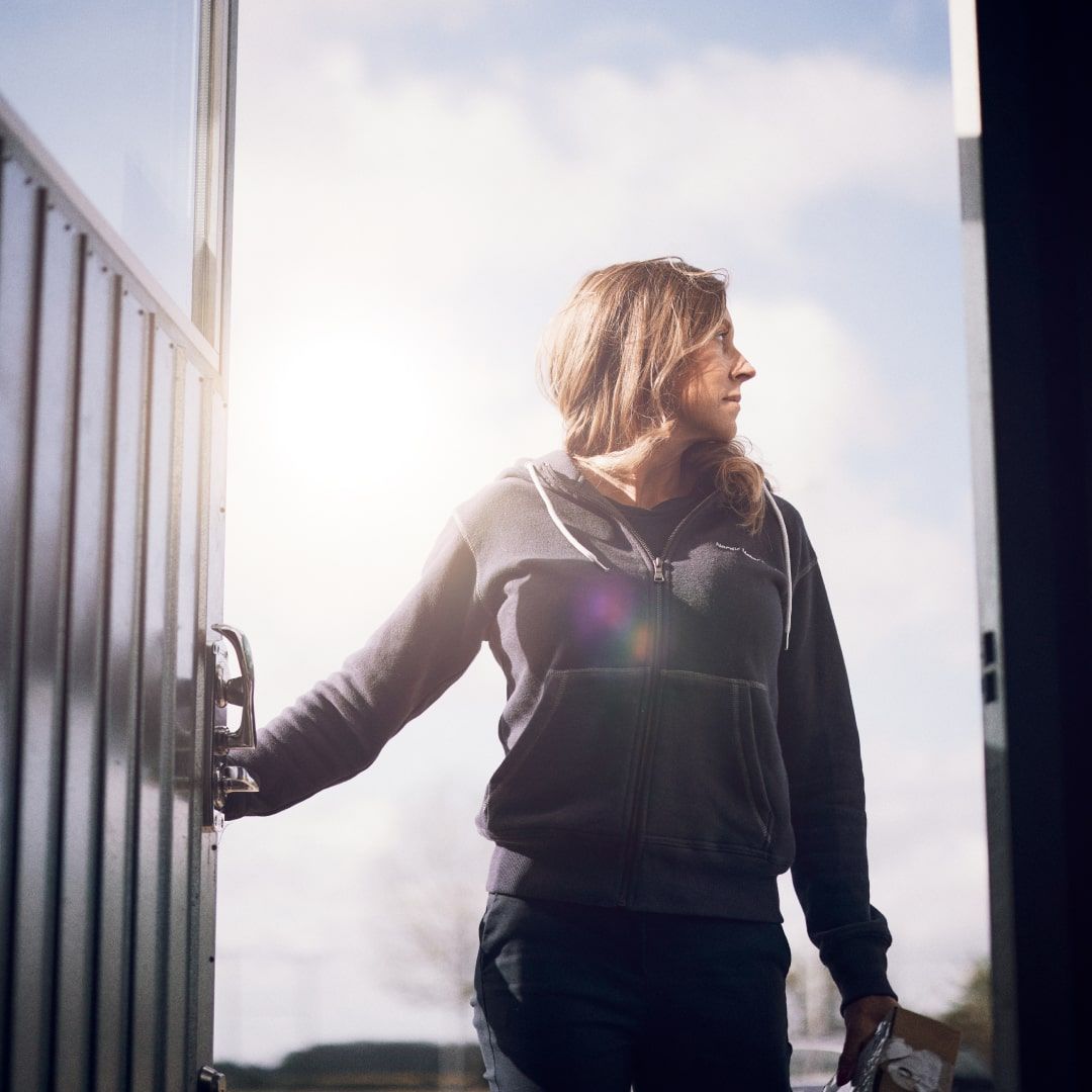 En kvinna öppnar en dörr, solljus lyser in