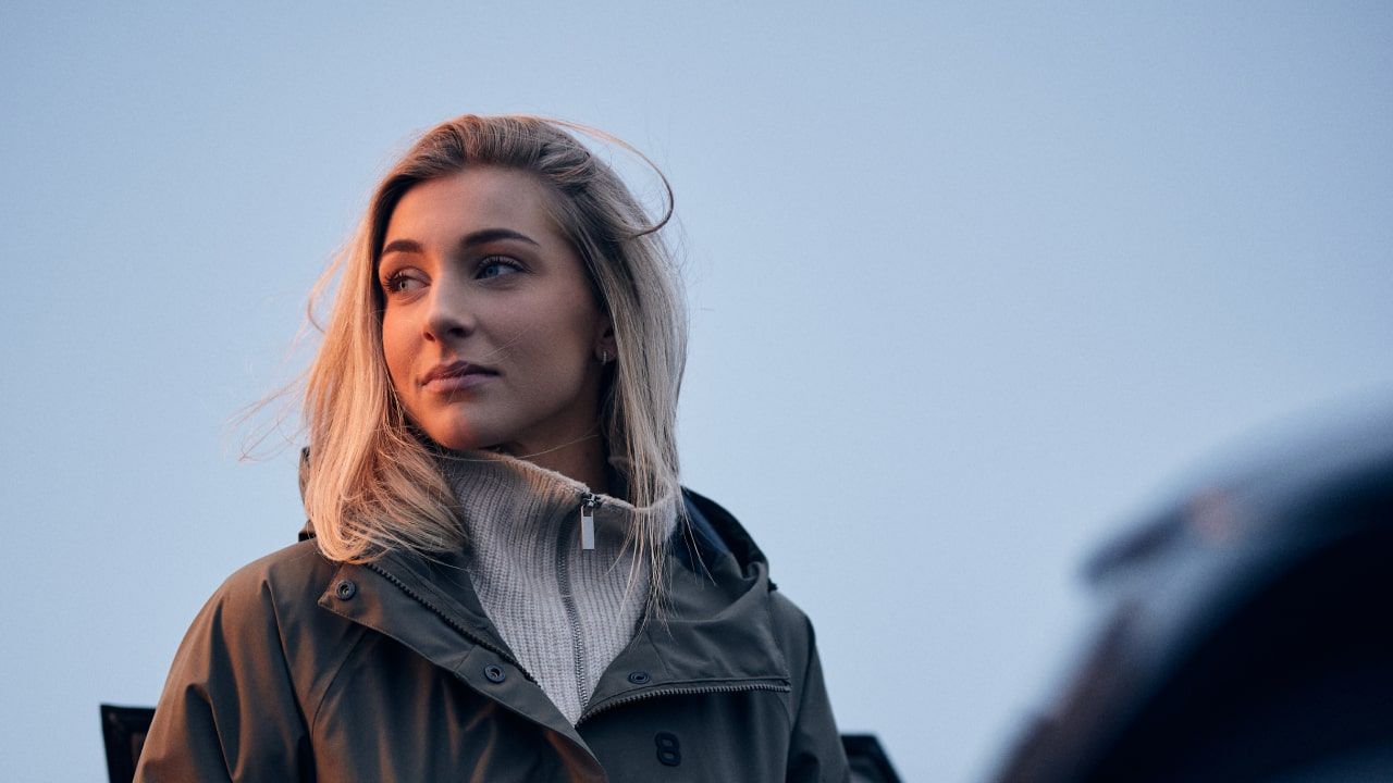 Porträtt på kvinna utomhus, skymningsljus och bil i förgrunden.