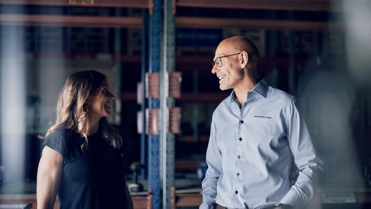 En kvinna och en man i en lagerlokal ler mot varandra i ett samtal